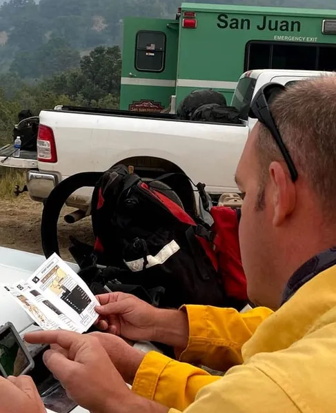 A wildland firefighter checking a phone on the hood of a truck at a fire camp