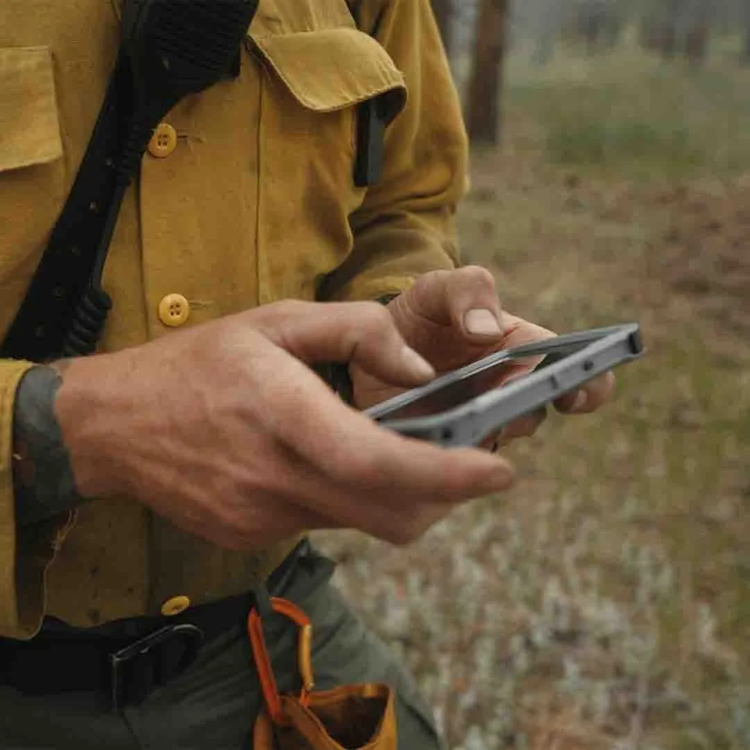 A wildland firefighter in a yellow shirt using a phone in the field